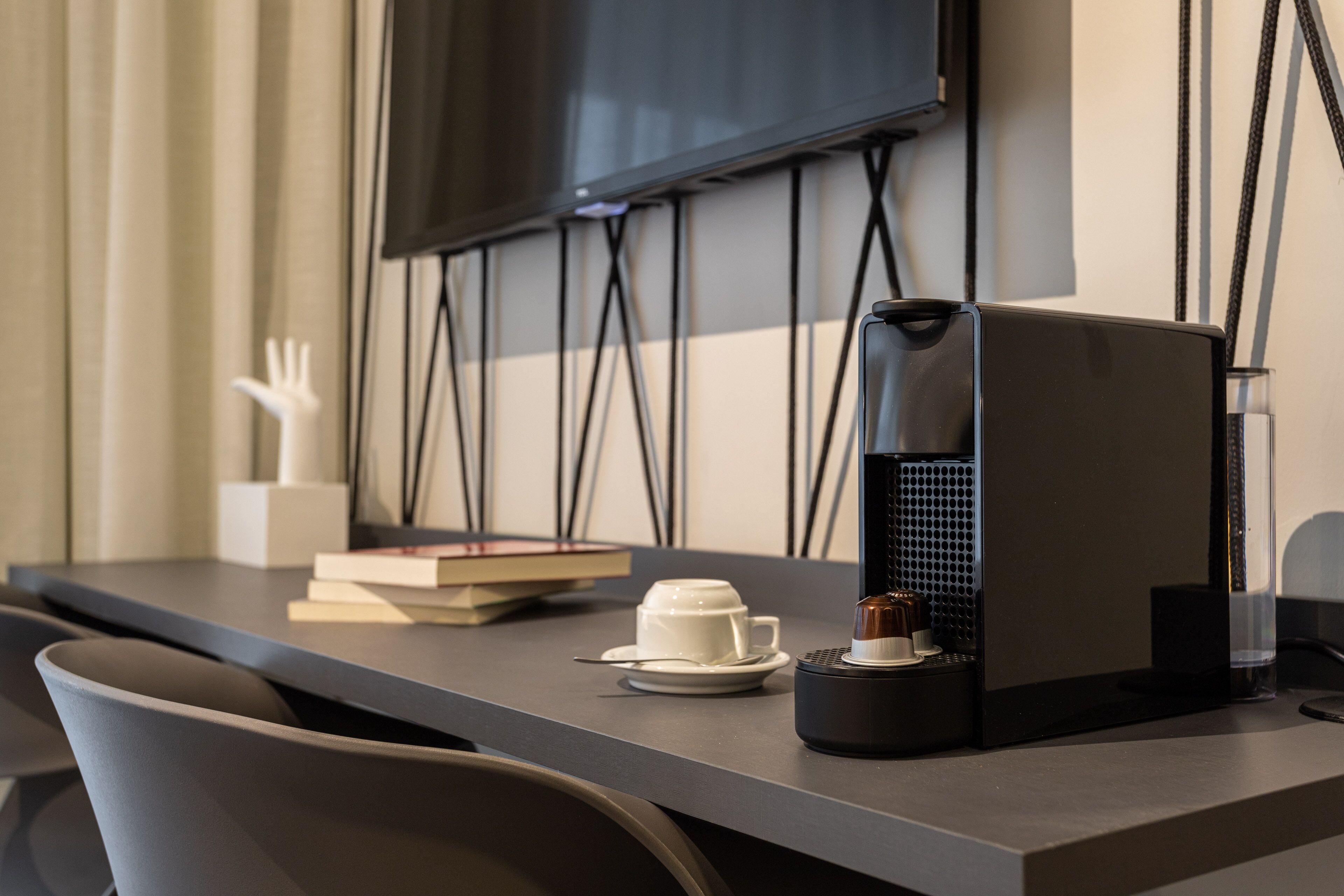 A modern hotel room with a flat-screen TV mounted on the wall, a coffee machine on the table, and a white decorative object.