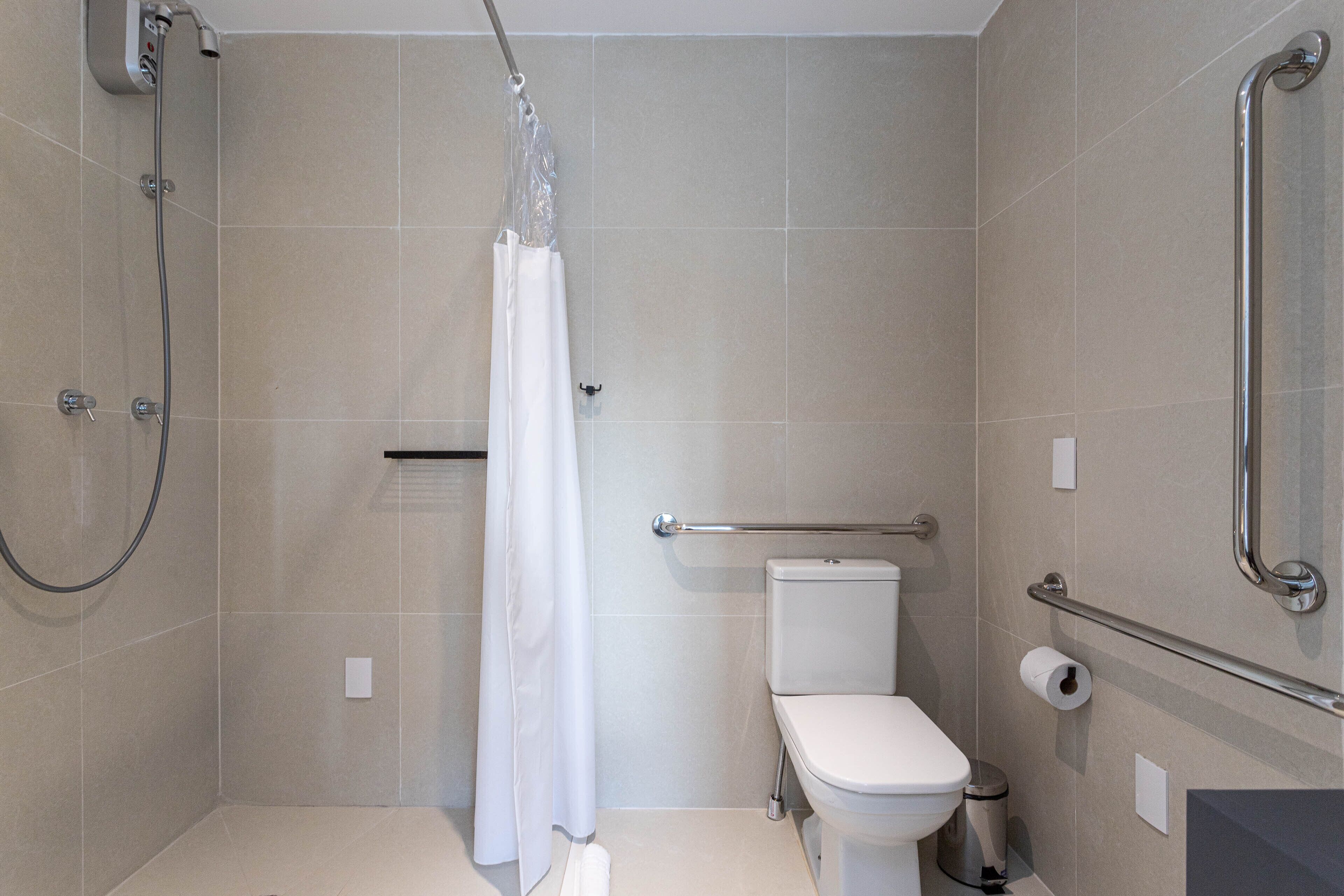 A modern bathroom with a shower, toilet, and grab bars.