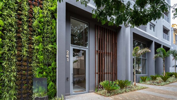 A modern building with a vertical garden, a glass door entrance, and a brick pathway.