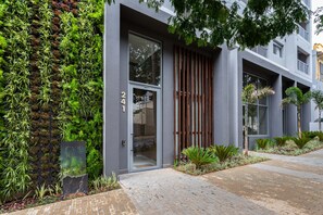 A modern building with a vertical garden, a glass door entrance, and a brick pathway.