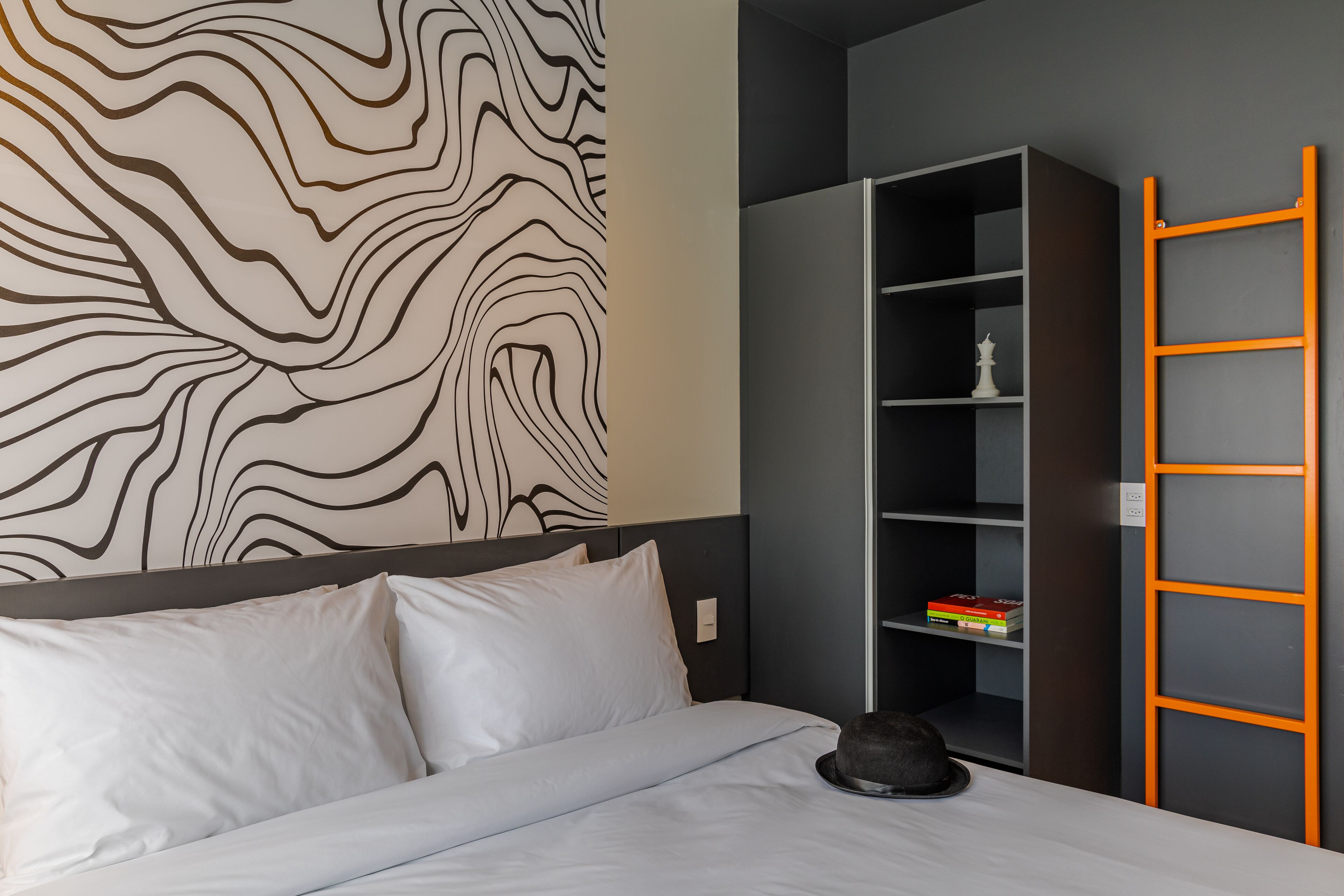 A hotel room with a bed, a bookshelf, and a wall with a wavy pattern.