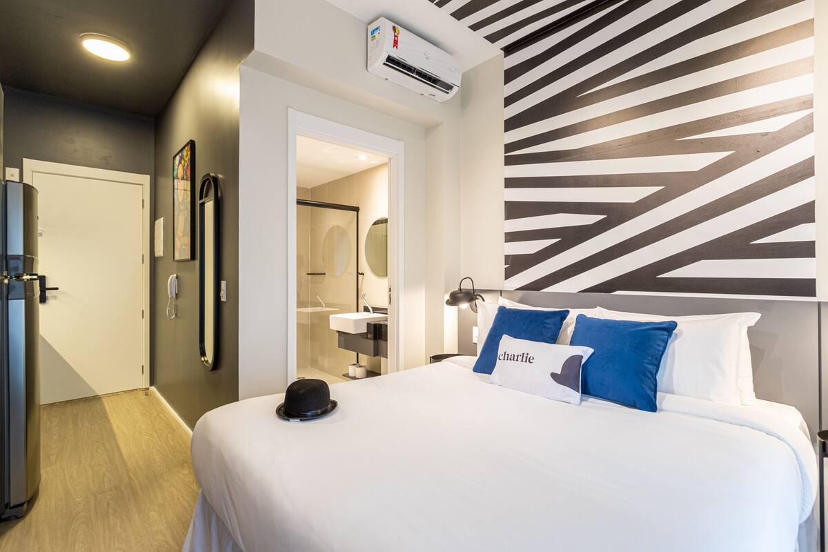 Een hotelkamer met een bed, een hoed op het bed, een badkamer met een wastafel en een spiegel.