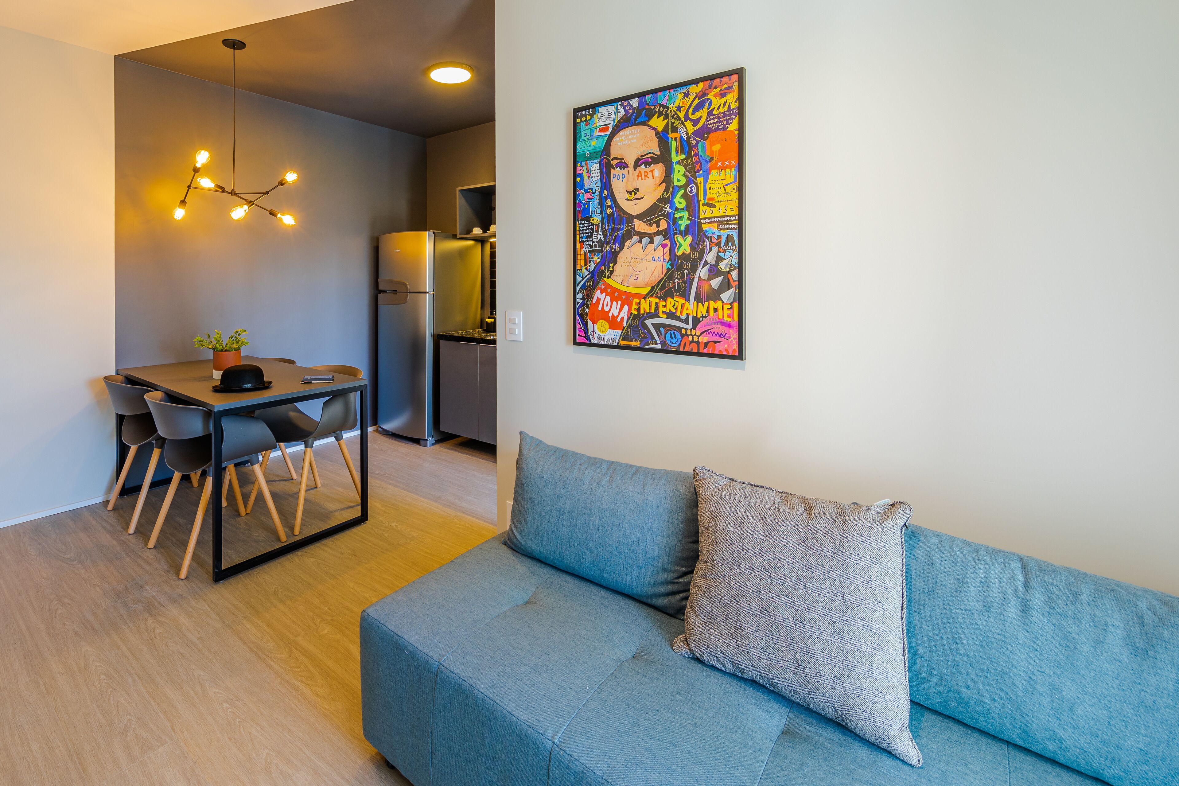 A modern living room with a blue sofa, a dining table with chairs, and a kitchen area in the background.