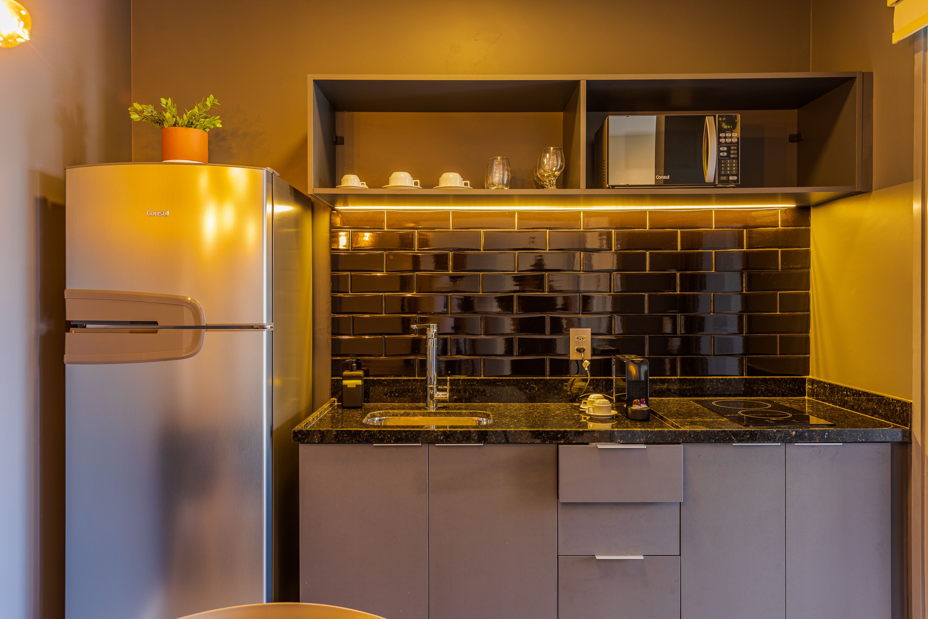 A modern kitchen with a built-in microwave, a stainless steel refrigerator, and a black tiled backsplash.
