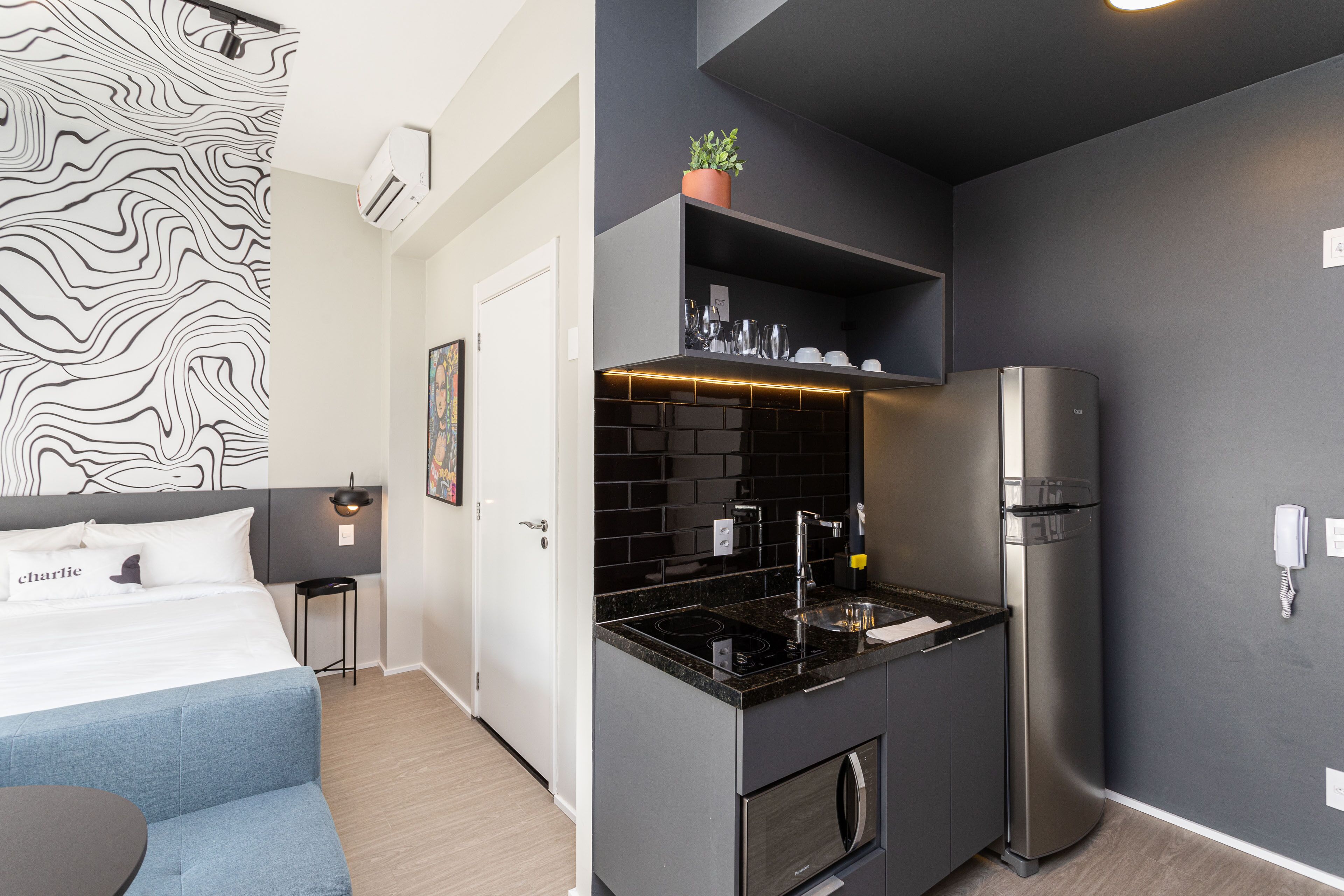A compact kitchen with a black countertop, stainless steel appliances, and a small potted plant on the shelf.