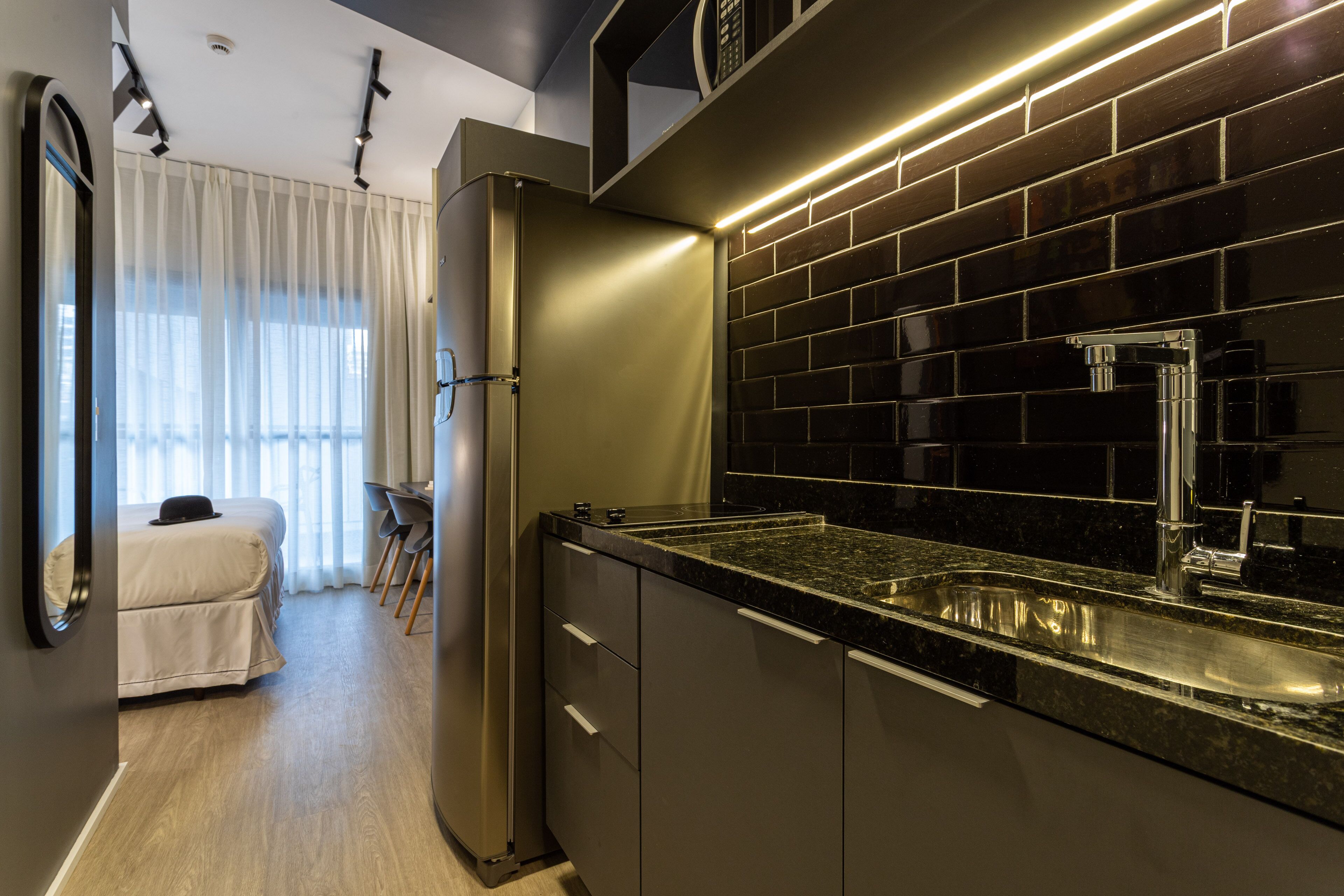 A modern kitchen with a black tiled backsplash, stainless steel sink, and a refrigerator.