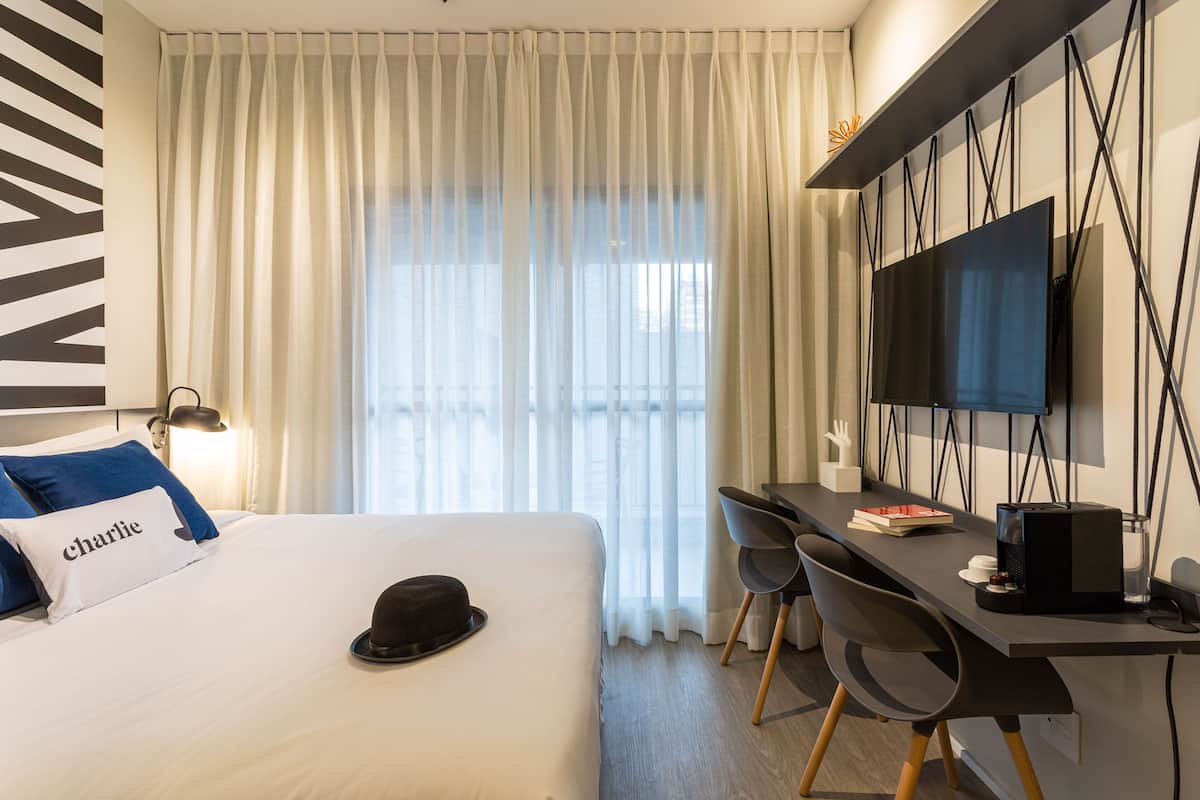 Een hotelkamer met een bed, een bureau met twee stoelen, een televisie en een raam met gordijnen.