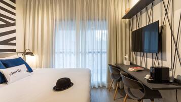A hotel room with a bed, a desk with two chairs, a television, and a window with curtains.
