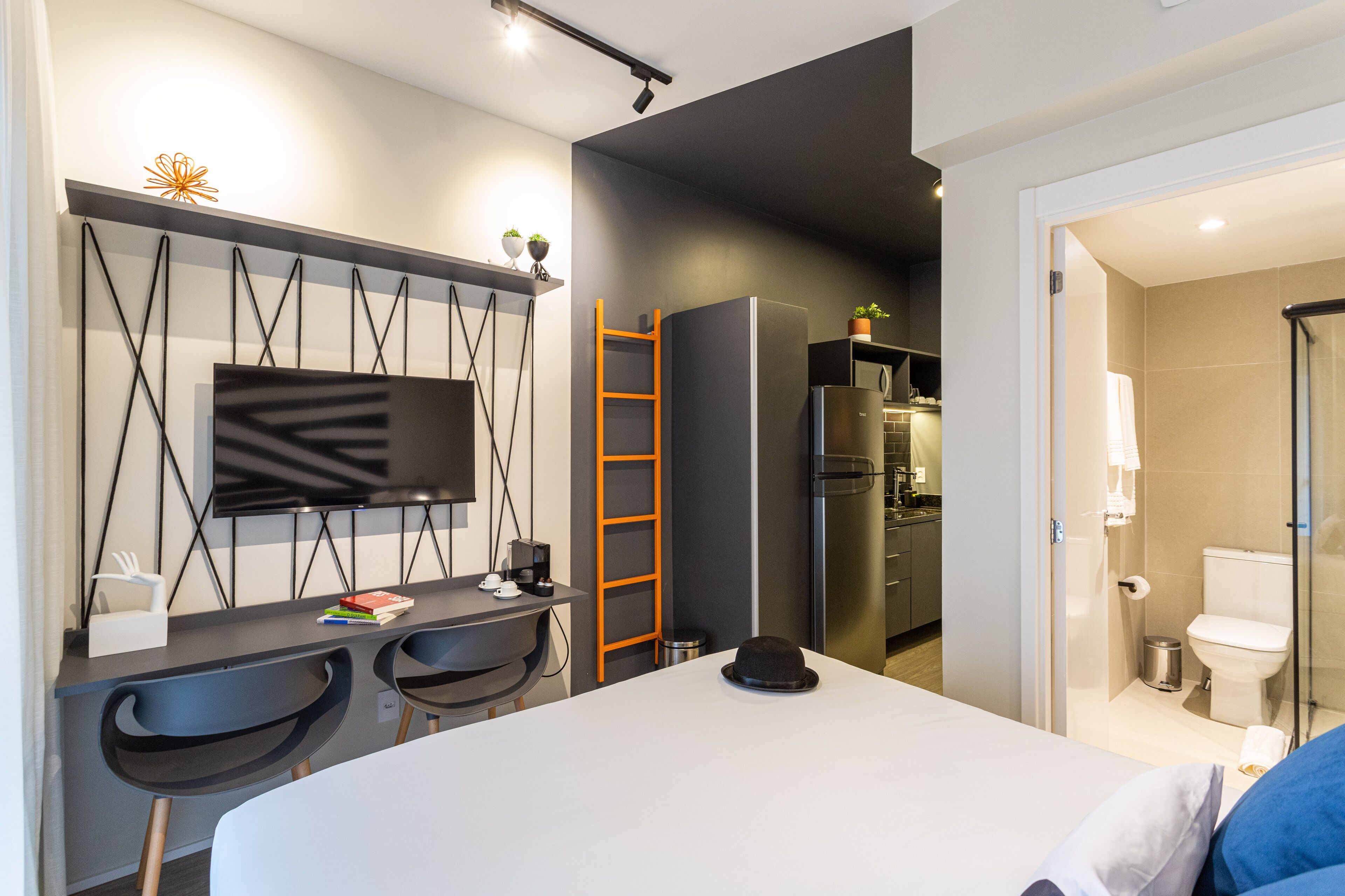 Een moderne hotelkamer met een bed, een bureau met twee stoelen, een televisie en een kitchenette.