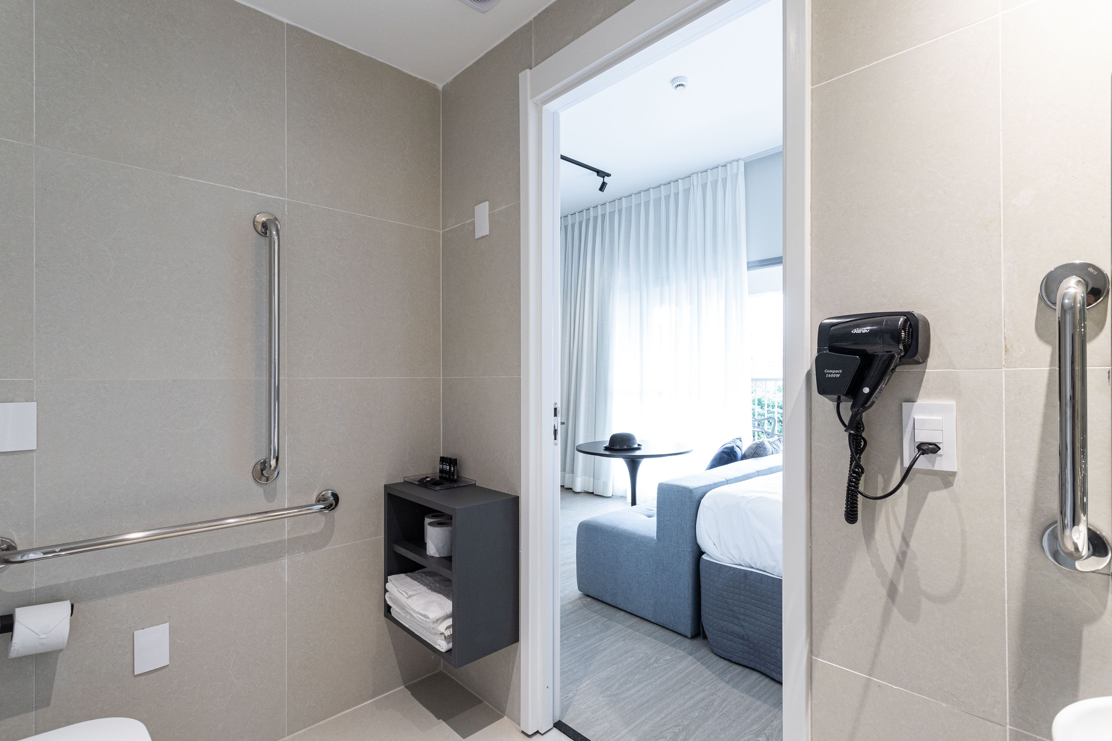 Un baño de hotel moderno con ducha, barras de apoyo, secador de pelo e inodoro.