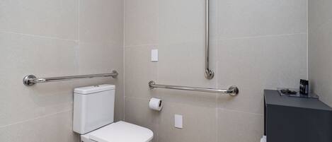 A modern bathroom with a toilet, grab bars, and a black sink.