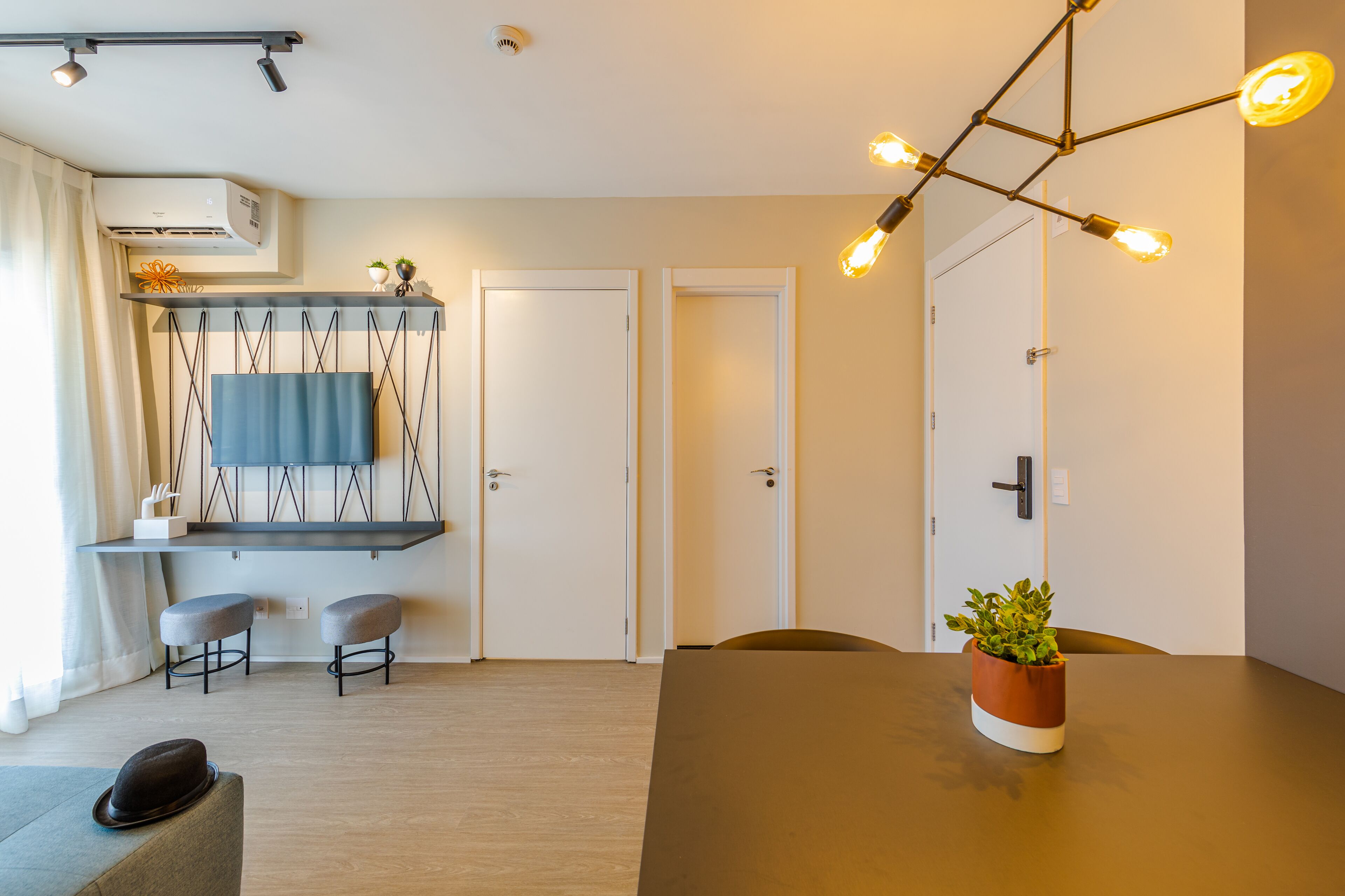 A modern hotel room with a dining area, a mounted TV, and a ceiling light fixture.