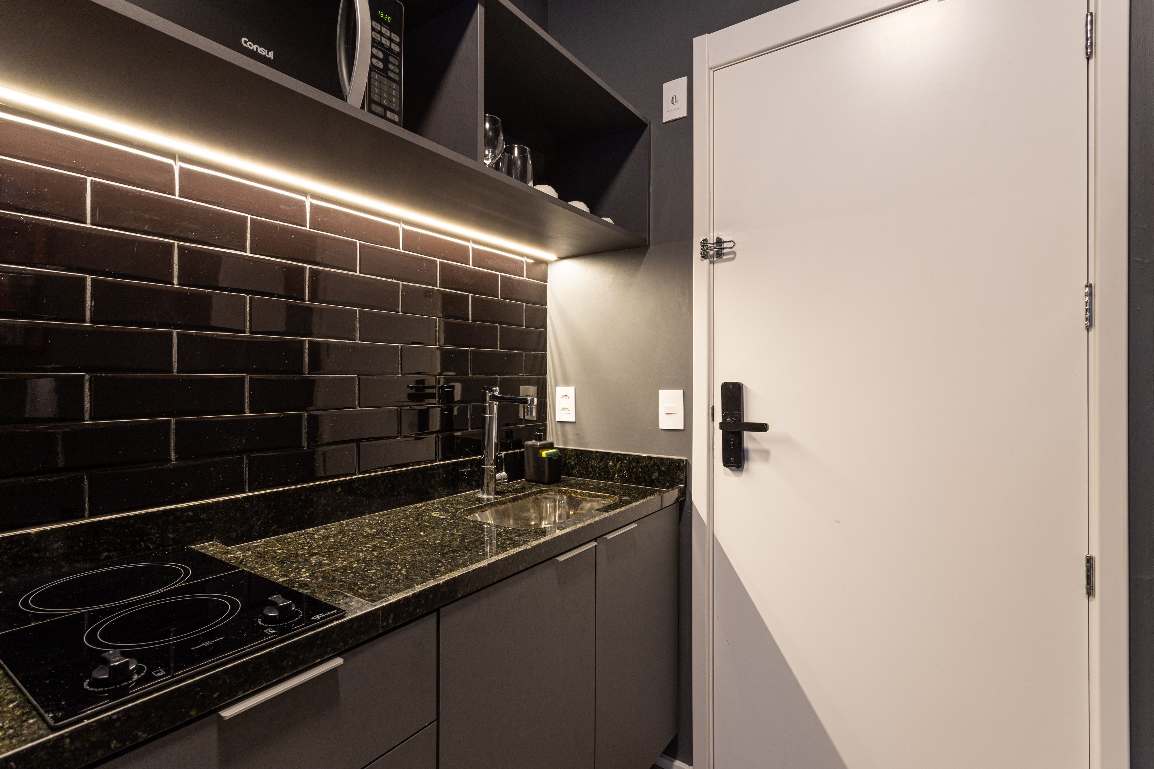 Une cuisine moderne avec un dosseret de carreaux noirs, des appareils en acier inoxydable et une porte blanche.