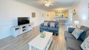 A spacious living room with a flat-screen TV, two sofas, a coffee table, and a ceiling fan. - Radiant and bright condo in the center of MB (Myrtle Beach)