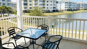 A balcony with a glass table and chairs, overlooking a body of water and a row of townhouses. - Radiant and bright condo in the center of MB (Myrtle Beach)