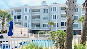 A multi-story hotel with a pool area, including lounge chairs and a small cabana. - Radiant and bright condo in the center of MB (Myrtle Beach)