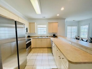 A modern kitchen with a stainless steel refrigerator, beige cabinets, a large island, and a window providing natural light.