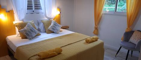 A neatly made bed with a yellow bedspread and pillows, a bedside table with a lamp, and a chair with a cushion.