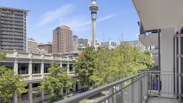 A high-rise building with a prominent tower in the background, surrounded by other buildings and trees.