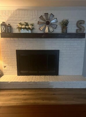 A white brick fireplace with a black mantel, a decorative clock, and a letter 'S' on the wall. - Spacious 5BR near Lake Conroe (Montgomery)