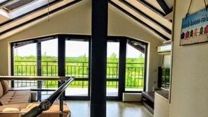 A spacious room with large windows offering a view of a green landscape. There is a sofa and a table with a chair.