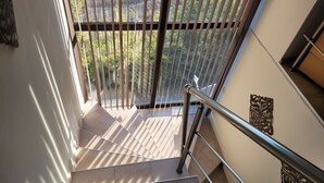 A staircase with a metal handrail and a view of greenery outside through vertical blinds.
