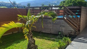 A patio area with a palm tree planter, a wooden staircase, and a view of mountains and a pool in the background. - Studio Ninirei (Papeete)