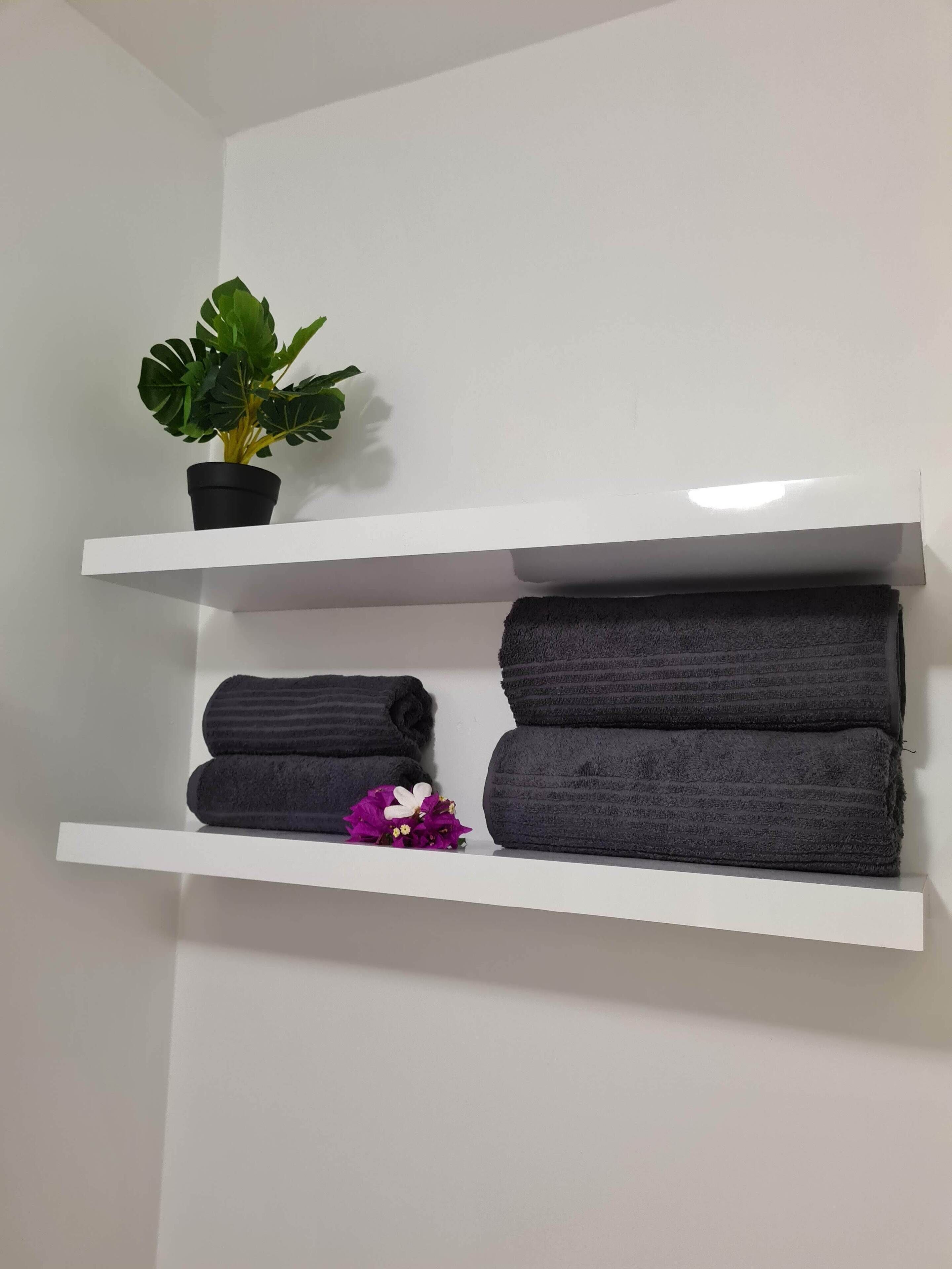 A white shelf with a potted plant and folded towels.