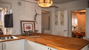 Una cocina con armarios blancos, encimera de madera, lámpara de araña y una obra de arte floral enmarcada.
