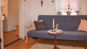 Una sala de estar acogedora con un sofá gris, una pequeña mesita de madera con una vela y una planta en maceta cerca de la ventana.