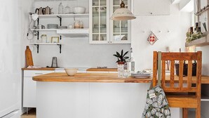 Una cocina con muebles blancos, una mesa de comedor de madera y una lámpara colgante.