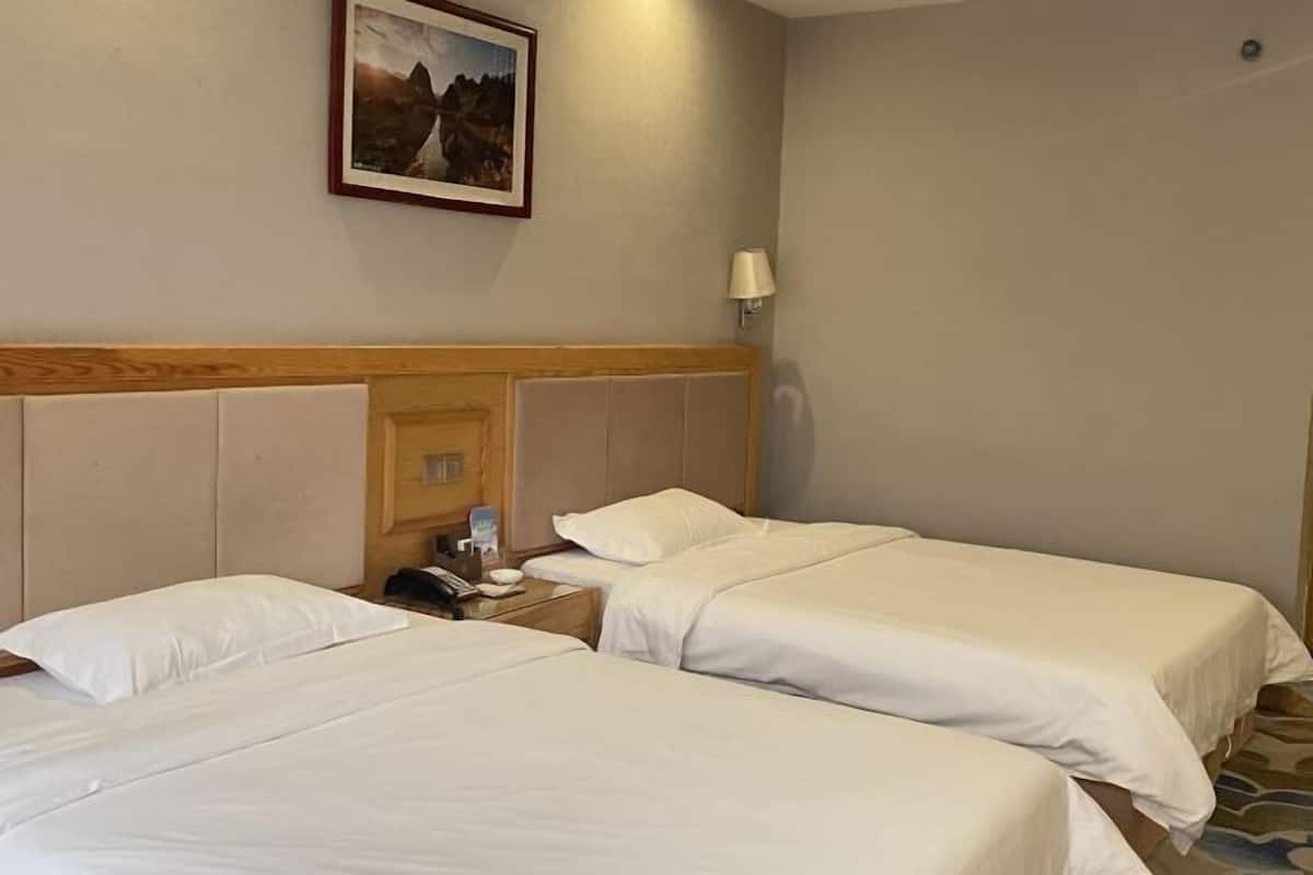 A hotel room with two single beds, a wooden headboard, a bedside table with a lamp, and a framed picture on the wall.
