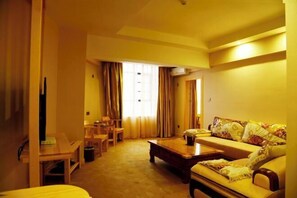 A hotel room with a sofa, a coffee table, a TV, and a window with curtains.