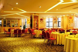 Un salón de banquetes con mesas redondas, sillas rojas y alfombra amarilla.