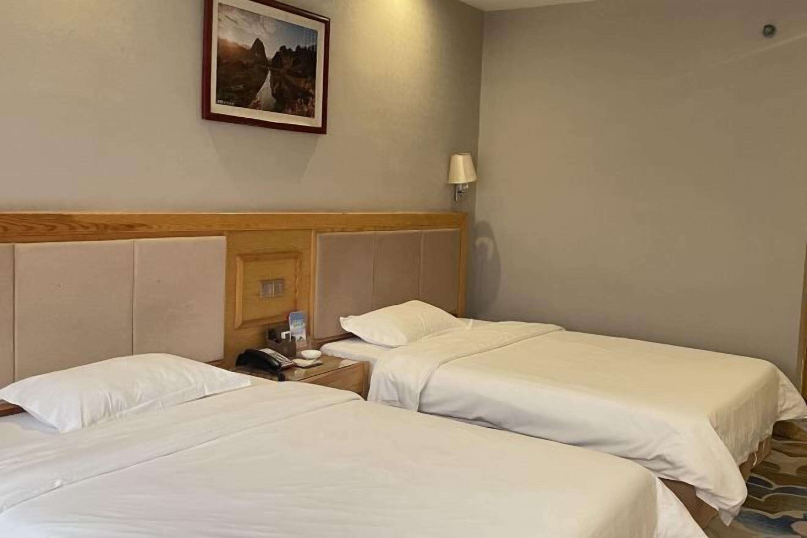 Una habitación de hotel con dos camas individuales, un cabecero de madera, una mesita de noche con una lámpara y un cuadro en la pared.
