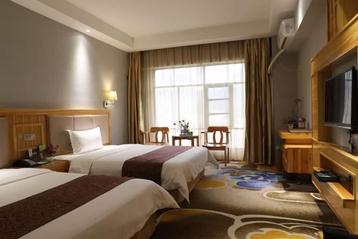 A hotel room with two beds, a TV, a desk, and a window with curtains.