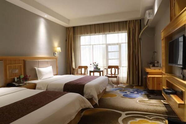A hotel room with two beds, a TV, a desk with a chair, and a large window with curtains.