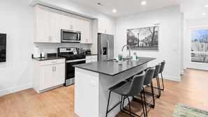 A modern kitchen with white cabinetry, stainless steel appliances, and a central island with bar stools.