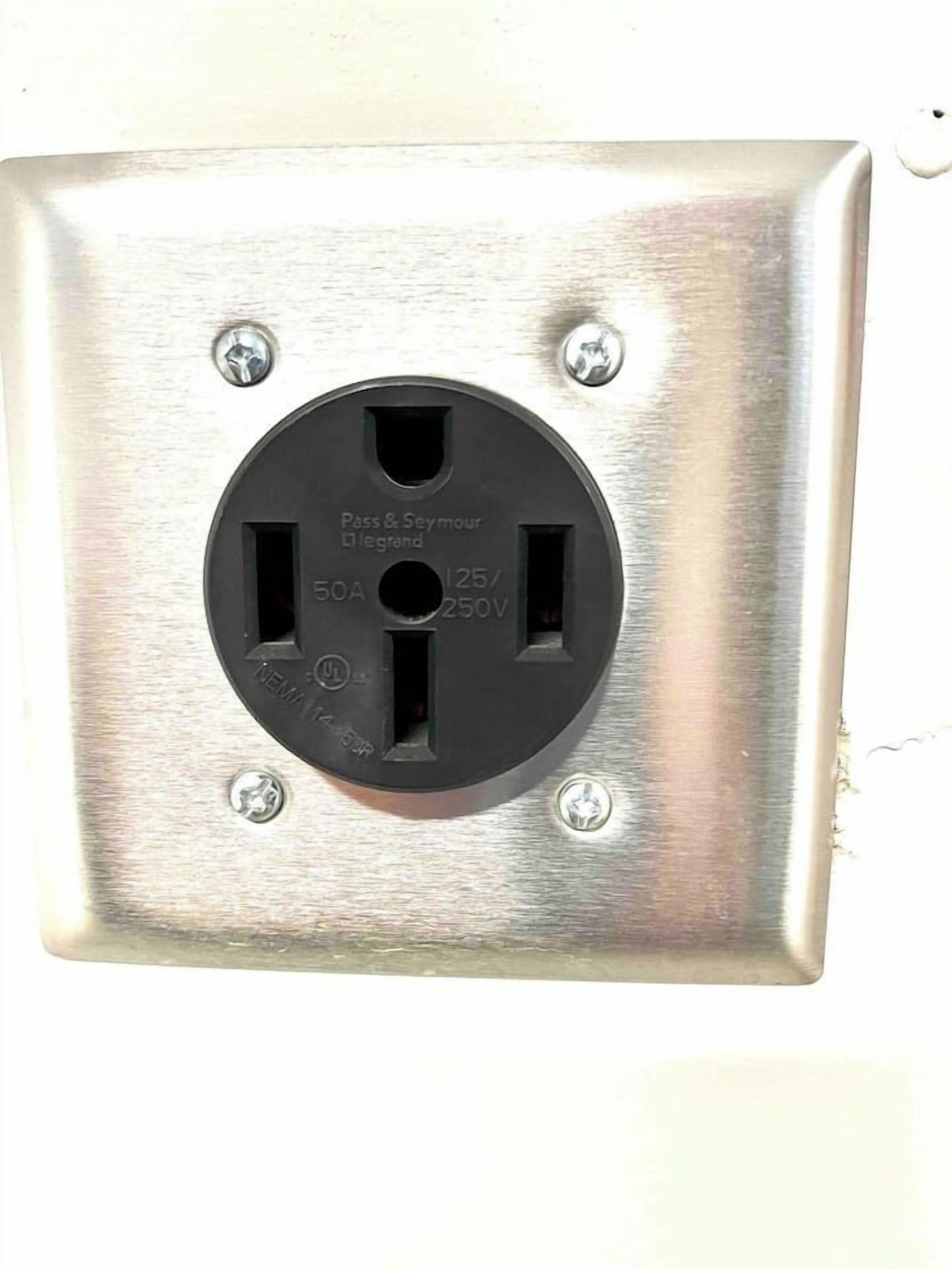 Una toma de corriente cuadrada con dos enchufes, una placa frontal negra y cuatro tornillos.