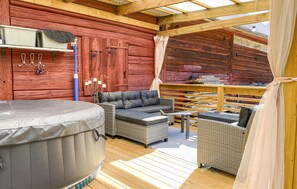 Un área de estar exterior acogedora con un jacuzzi, muebles de mimbre y una terraza de madera.