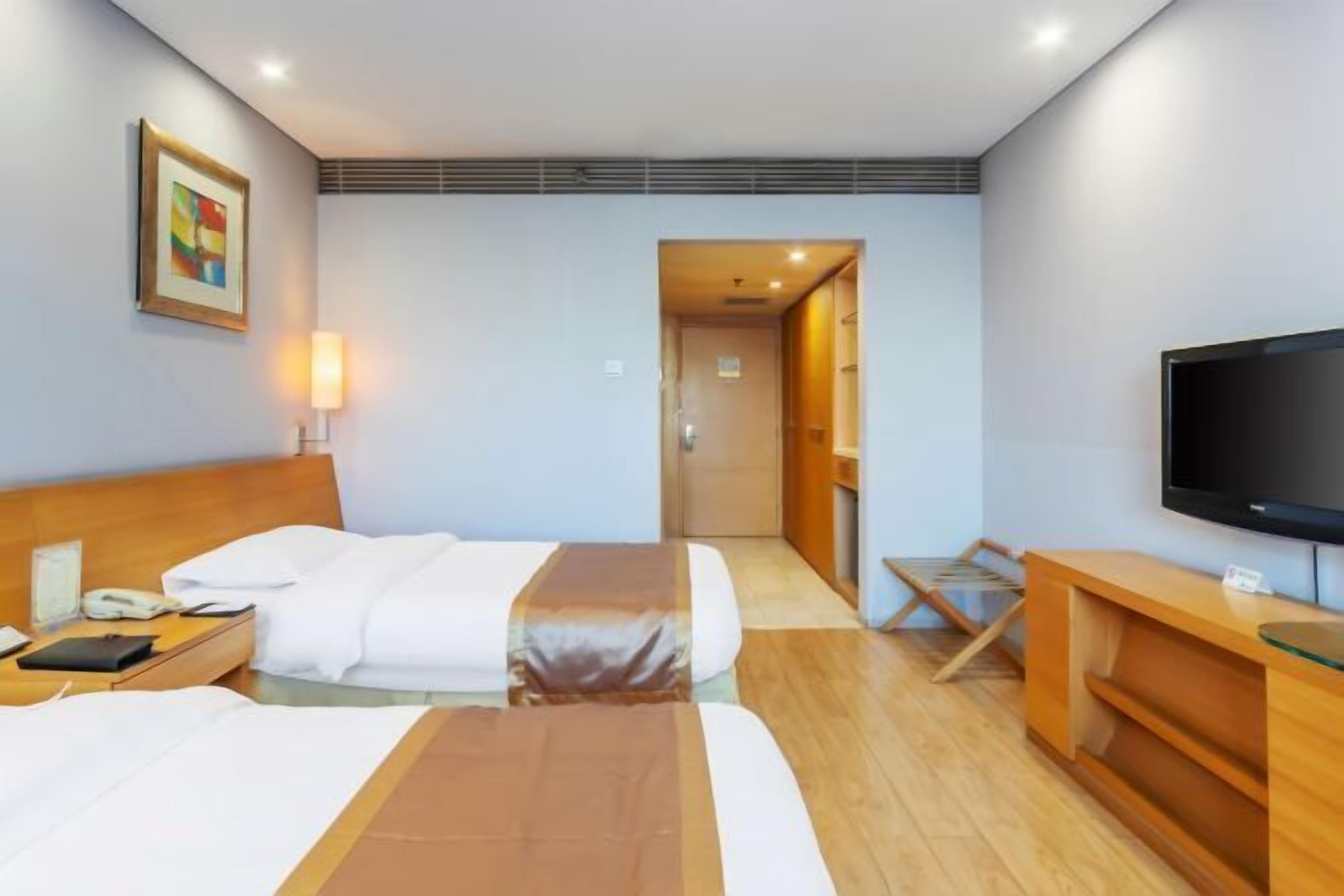 Hotellihuone, jossa on kaksi sänkyä, televisio, työpöytä ja taulu seinällä.
