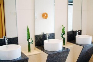 A modern bathroom with three round white sinks, dark granite countertops, and a mirror with a wooden panel. - Qiangang Hotel (Qian'an)