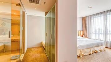 Hotellihuone, jossa on lasiseinä, beigenvärinen peitto sängyllä ja suuri ikkuna, jossa on verhot.