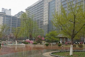 A courtyard with trees, a white fence, and a building in the background. - Qiangang Hotel (Qian'an)