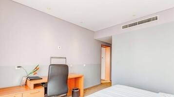 Une chambre d’hôtel comprenant un lit, un bureau avec une chaise, une petite table, une poubelle et une porte donnant sur une autre pièce.