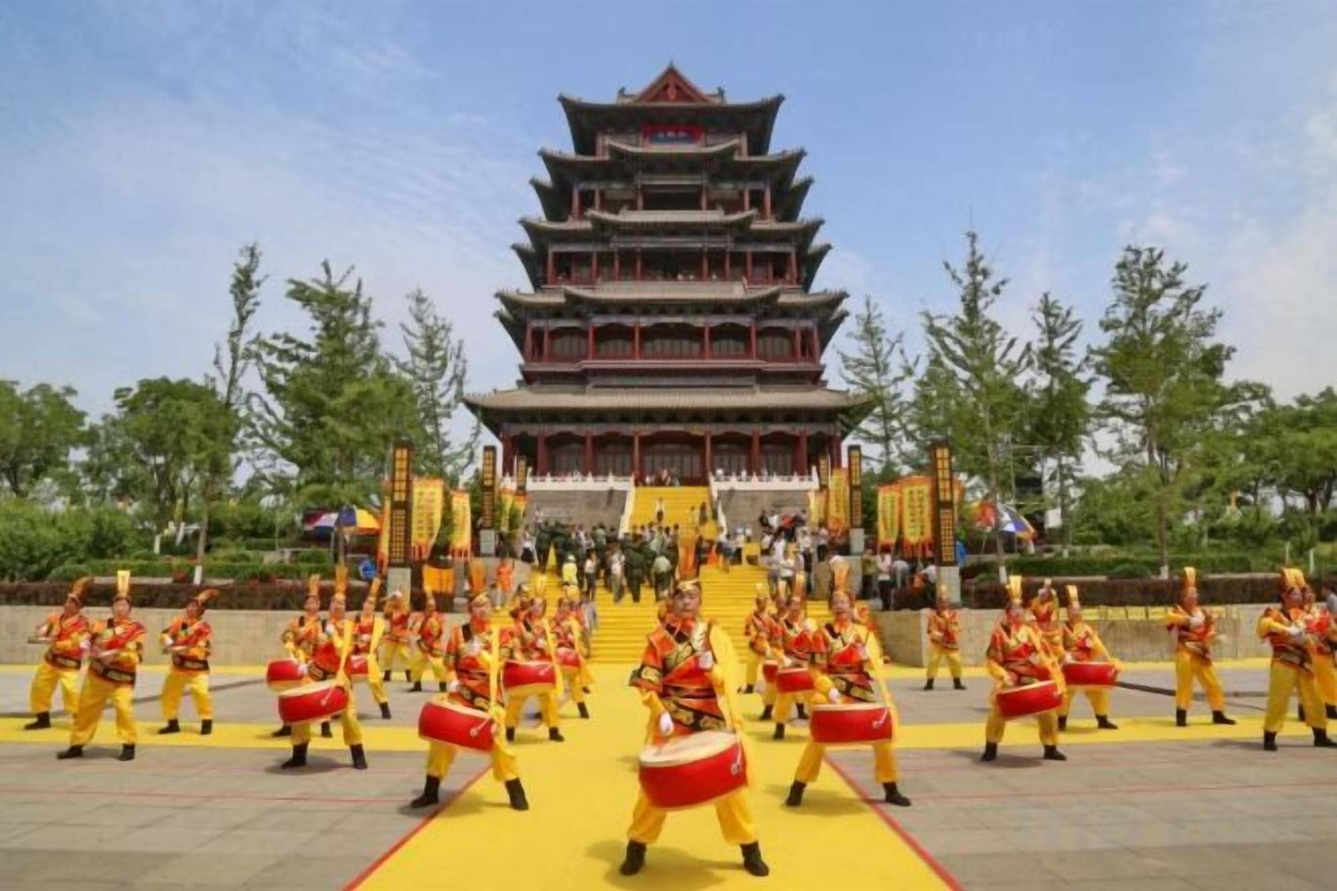 Un edificio tradicional con tejado escalonado, rodeado de artistas vestidos de amarillo y rojo.