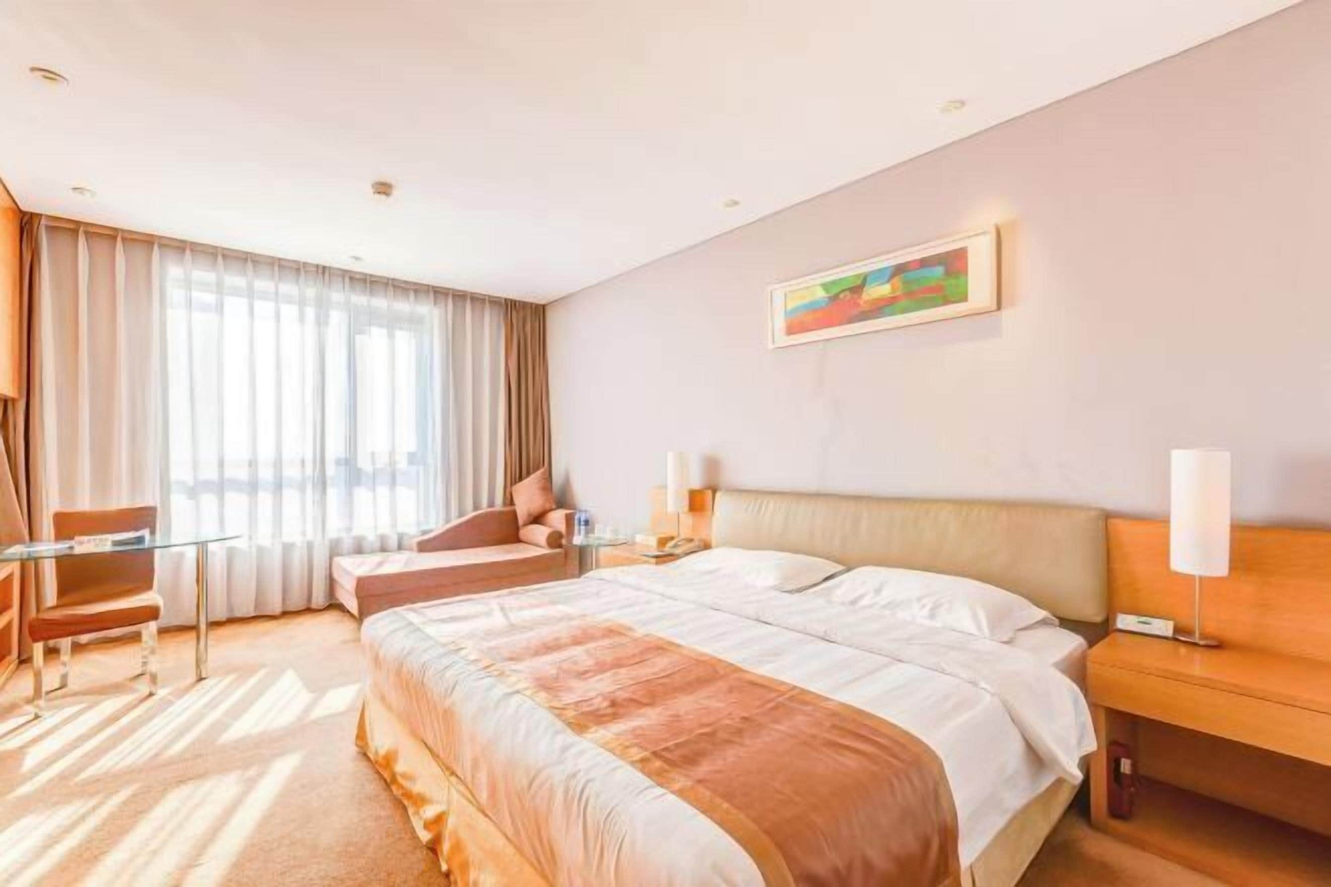 Une chambre d’hôtel avec un lit, un bureau, une chaise, une table de chevet, une lampe et un tableau au mur.