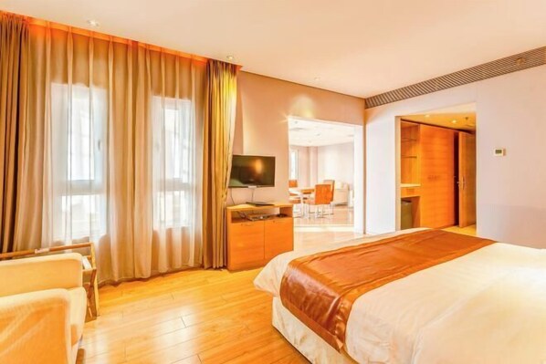 A hotel room with a large bed, a desk with a computer, a TV, and a view of the hallway. - Qiangang Hotel (Qian'an)