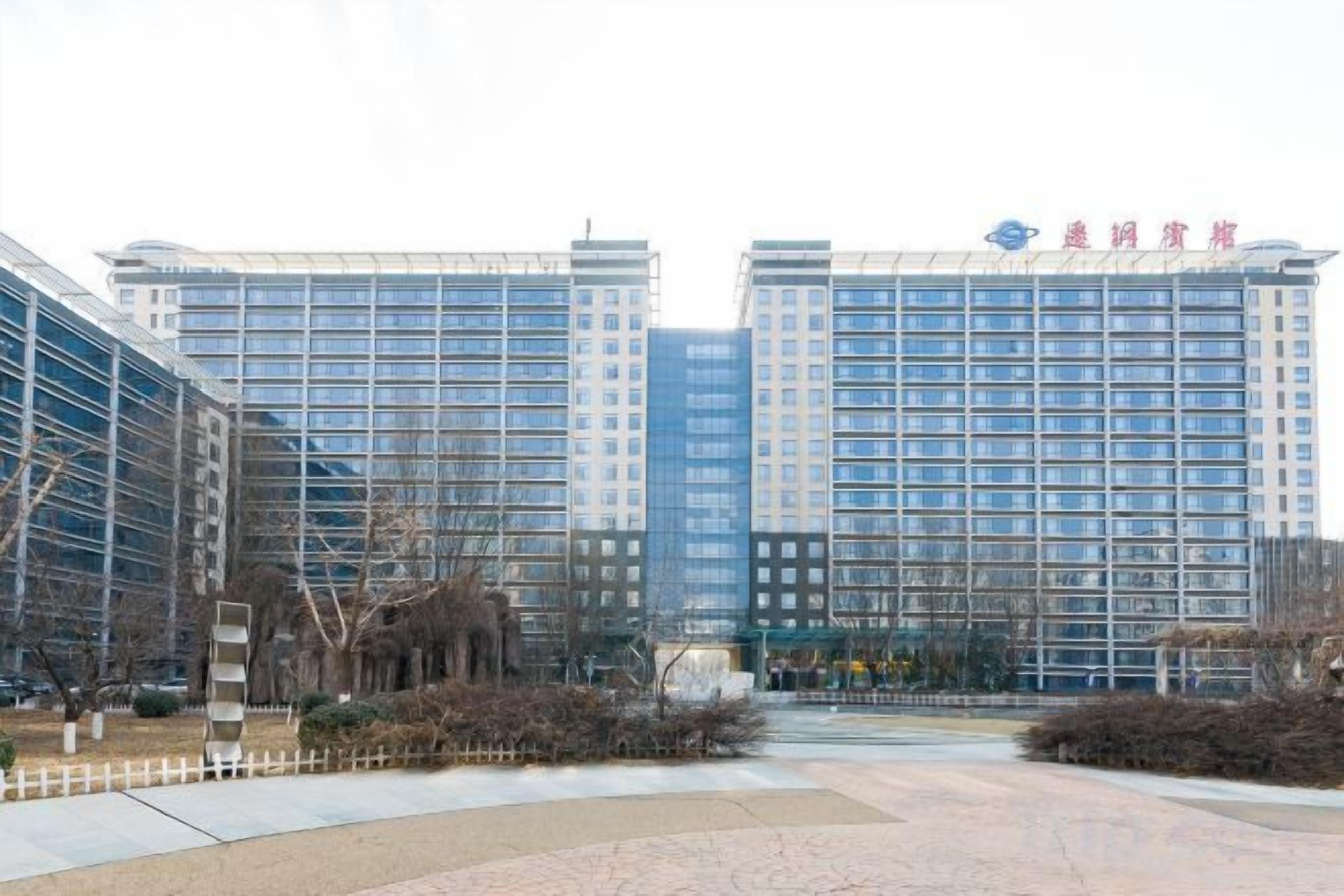 A multi-story hotel with a modern facade, a central courtyard, and a clear sky.