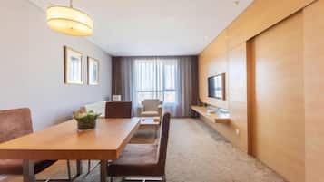 Une chambre d’hôtel avec une table à manger en bois, un canapé, un téléviseur posé sur un meuble et une grande fenêtre avec des rideaux.